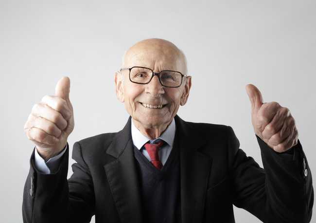 An elderly man in a suit giving two thumbs up