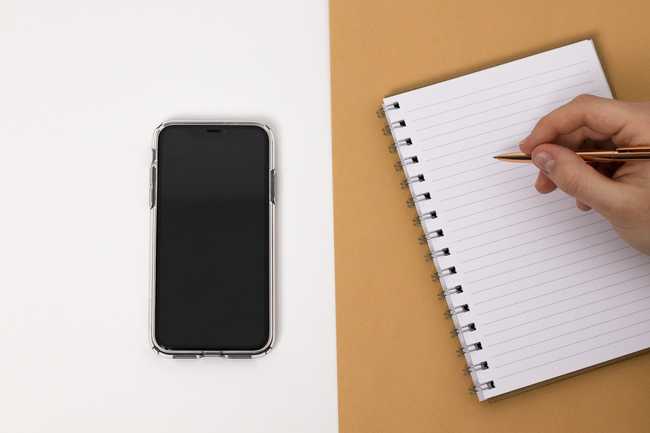 A Cell Phone and person Writing in a Notebook