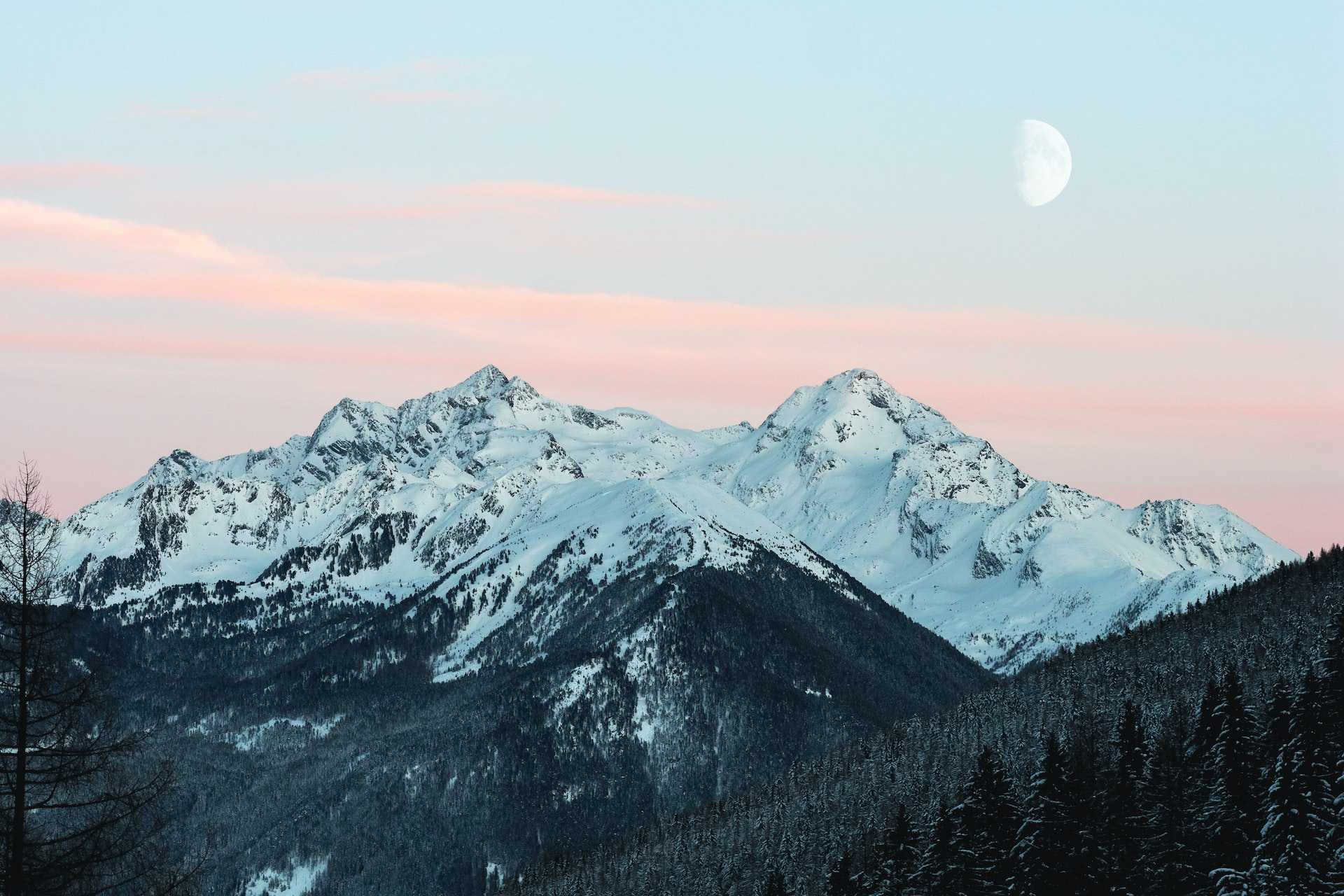 Snow capped mountain range at early sunset with the moon visible