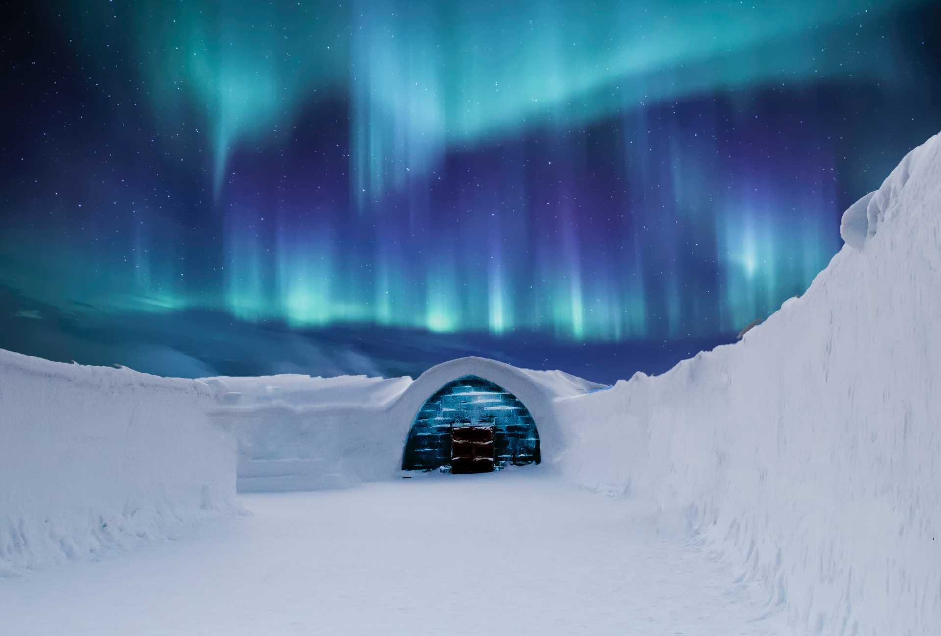 Aurora Borealis over a snow covered path leading to an igloo-like structure.